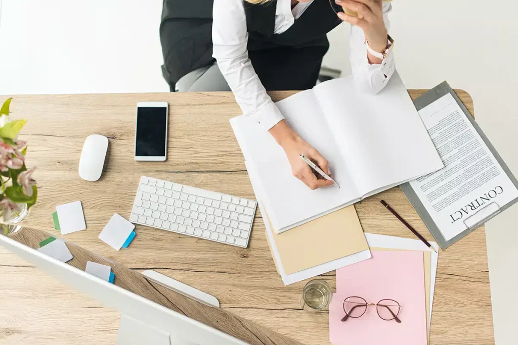 Woman sitting in front of her computer with papers and notebooks on her desk, planning a hybrid membership and course model