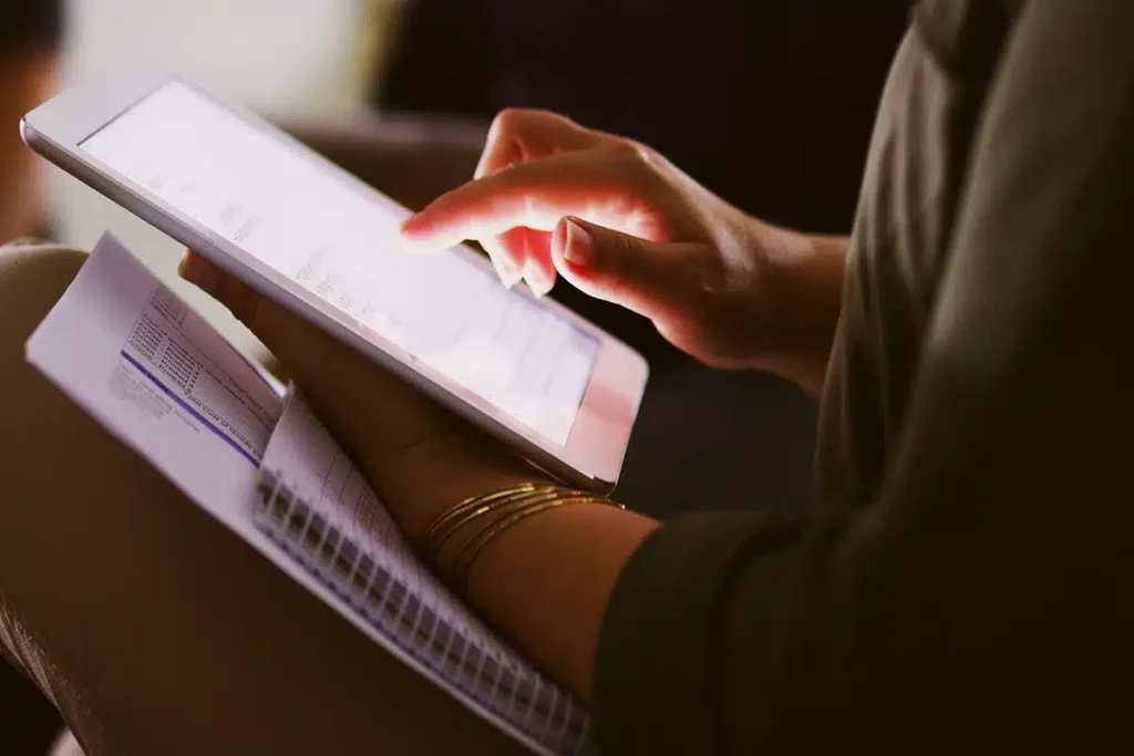 A person using a tablet and holding notes, illustrating the process and benefits of creating digital courses